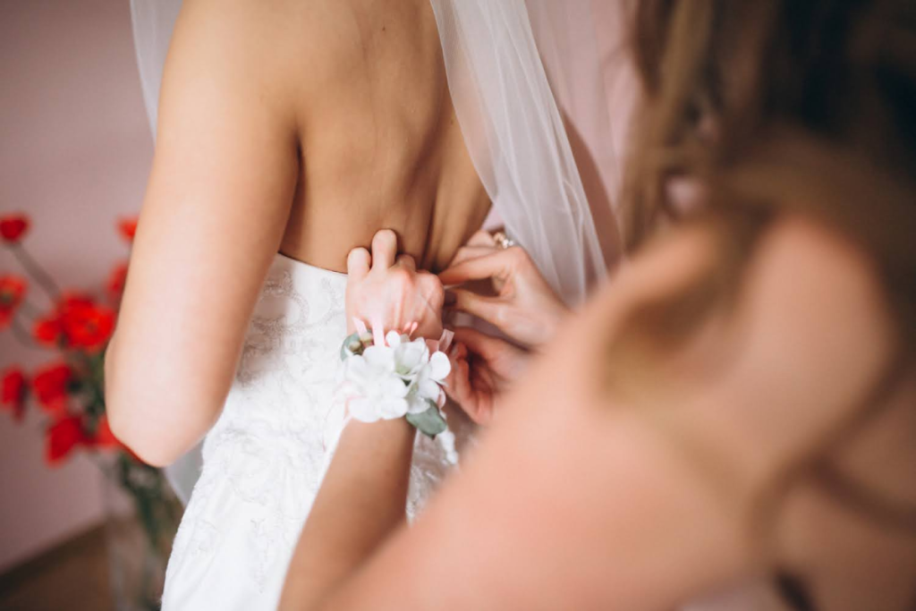 Close-up of a bridesmaid adjusting the back of the bride’s wedding dress.