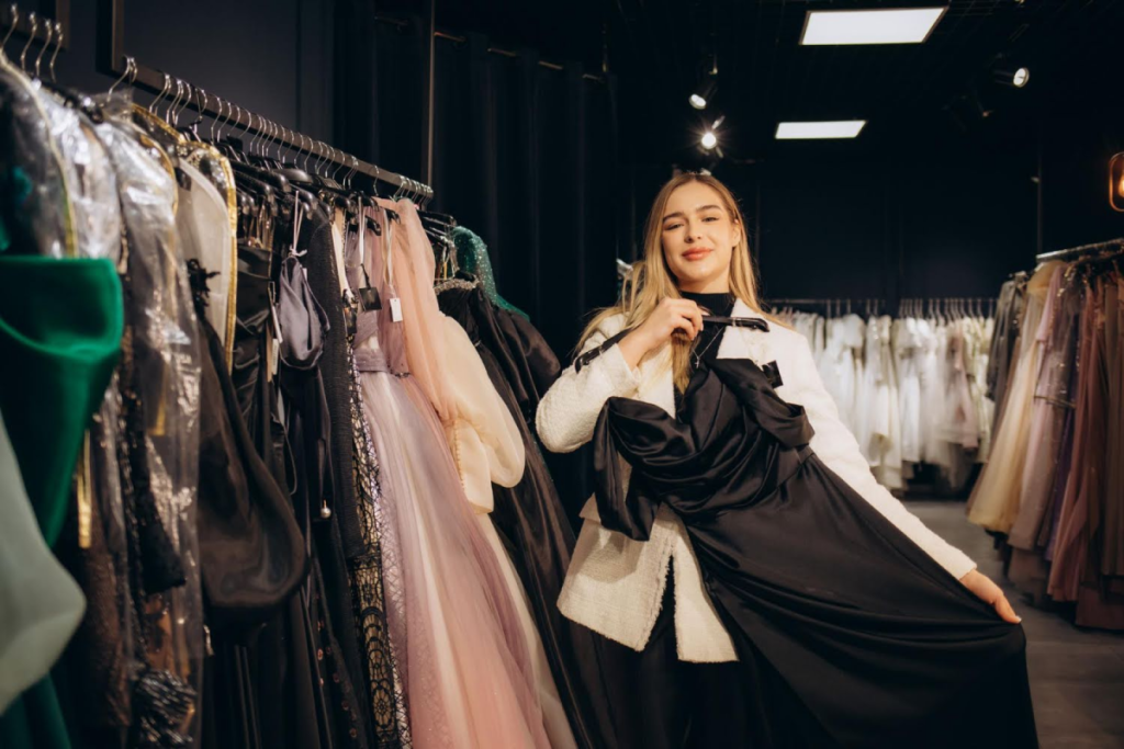 Bridesmaid in a boutique holding a black gown surrounded by other elegant dresses.