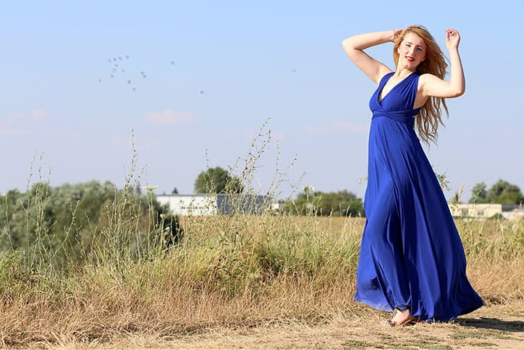 Bridesmaid wearing a flowing blue dress, standing in a field under a clear sky.