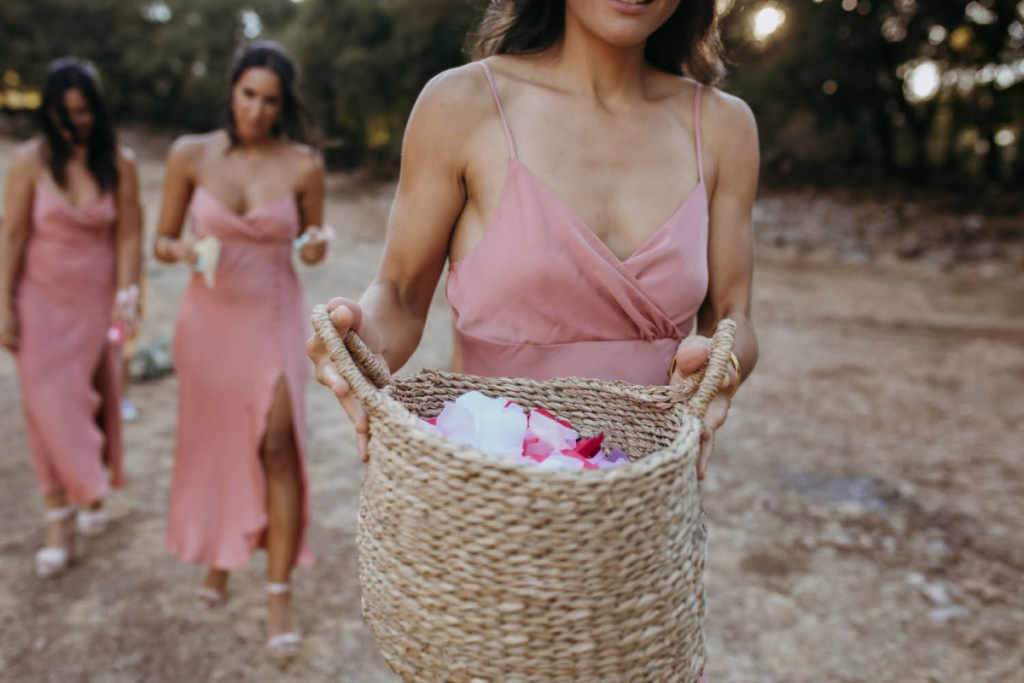 A bridesmaid holding a basket filled with rose petals, followed by two others in blush dresses.