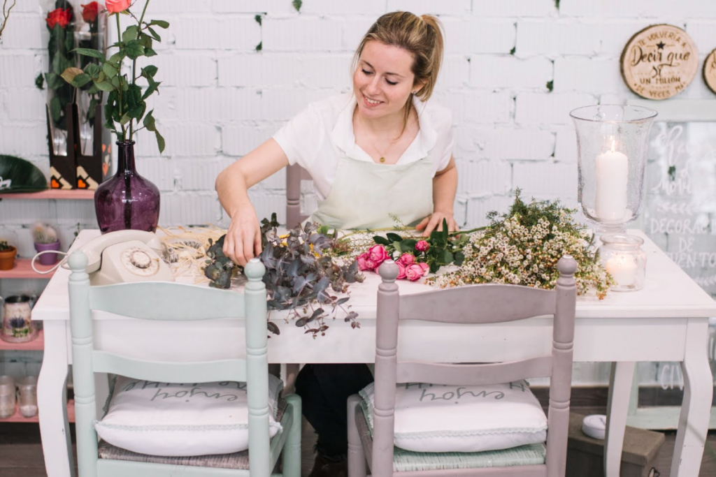 Florist arranging wedding flowers at a table with vases and greenery.