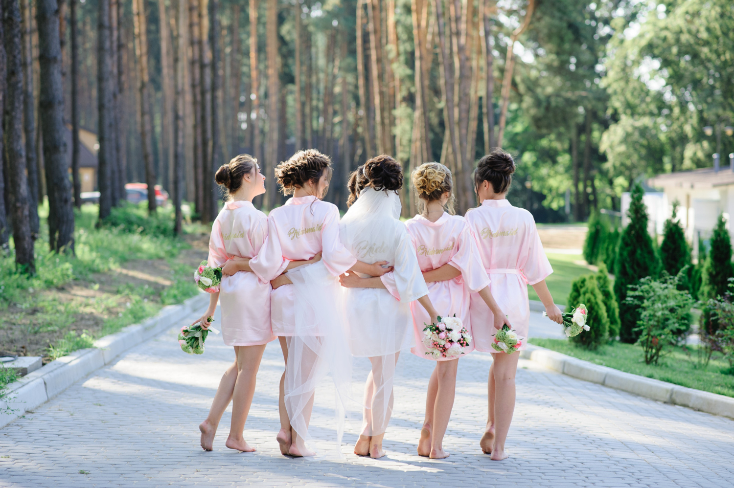 Bridesmaids in pink robes outdoors.